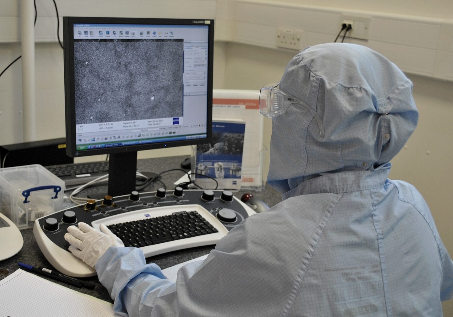 A researcher in cleanroom clothing working at an analysis workstation