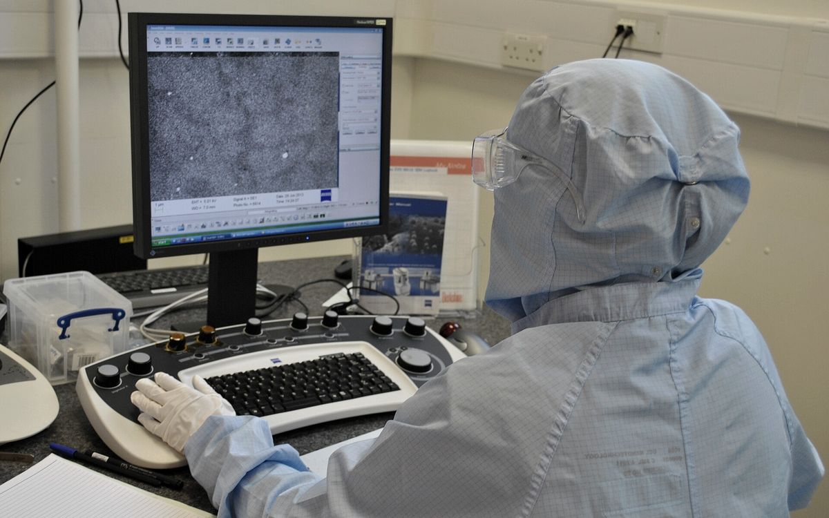 A researcher in cleanroom clothing at an analysis workstation